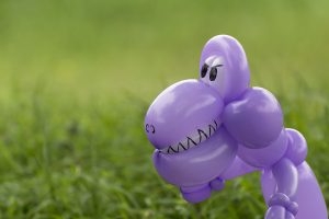 Closeup of purple balloon animal dinosaur with teeth and eyes looking scary in the lush green grass of a back yard in Euless, Texas