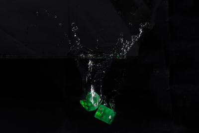 Water droplets and splash from two green dice being dropped into water