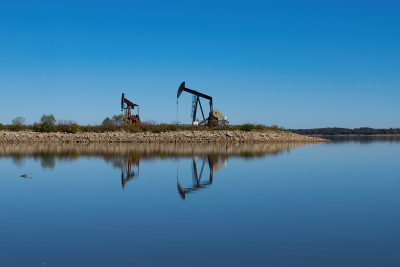 Pair of oil pump jacks on rocky peninsula in glassy calm lake