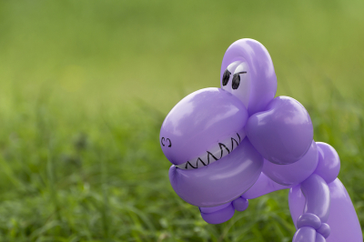 Closeup of purple balloon animal dinosaur in green grass of back yard