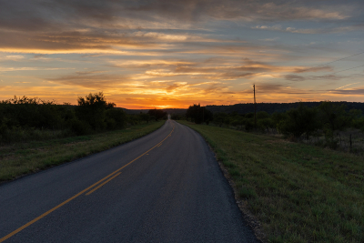 Rural country road leading to a beautiful orange sky at sunset