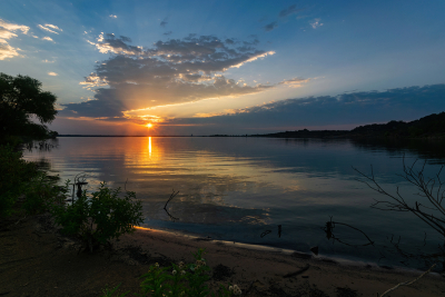 Sun peeking below clouds at sunrise over a calm lake